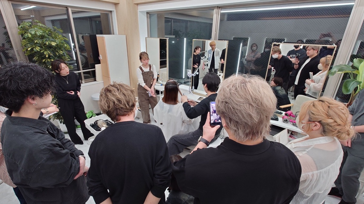 会場のワイドショット。モデルを囲んでカット実演を見学する美容師たち